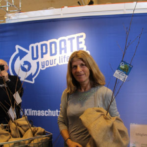 Mybluetree Event Frau zeigt Setzling im Jutesack blau Hintergrund