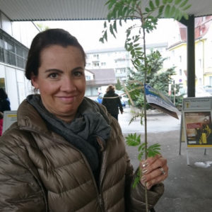 Mybluetree Event Frau präsentiert Baum Setzling und schaut in Kamera