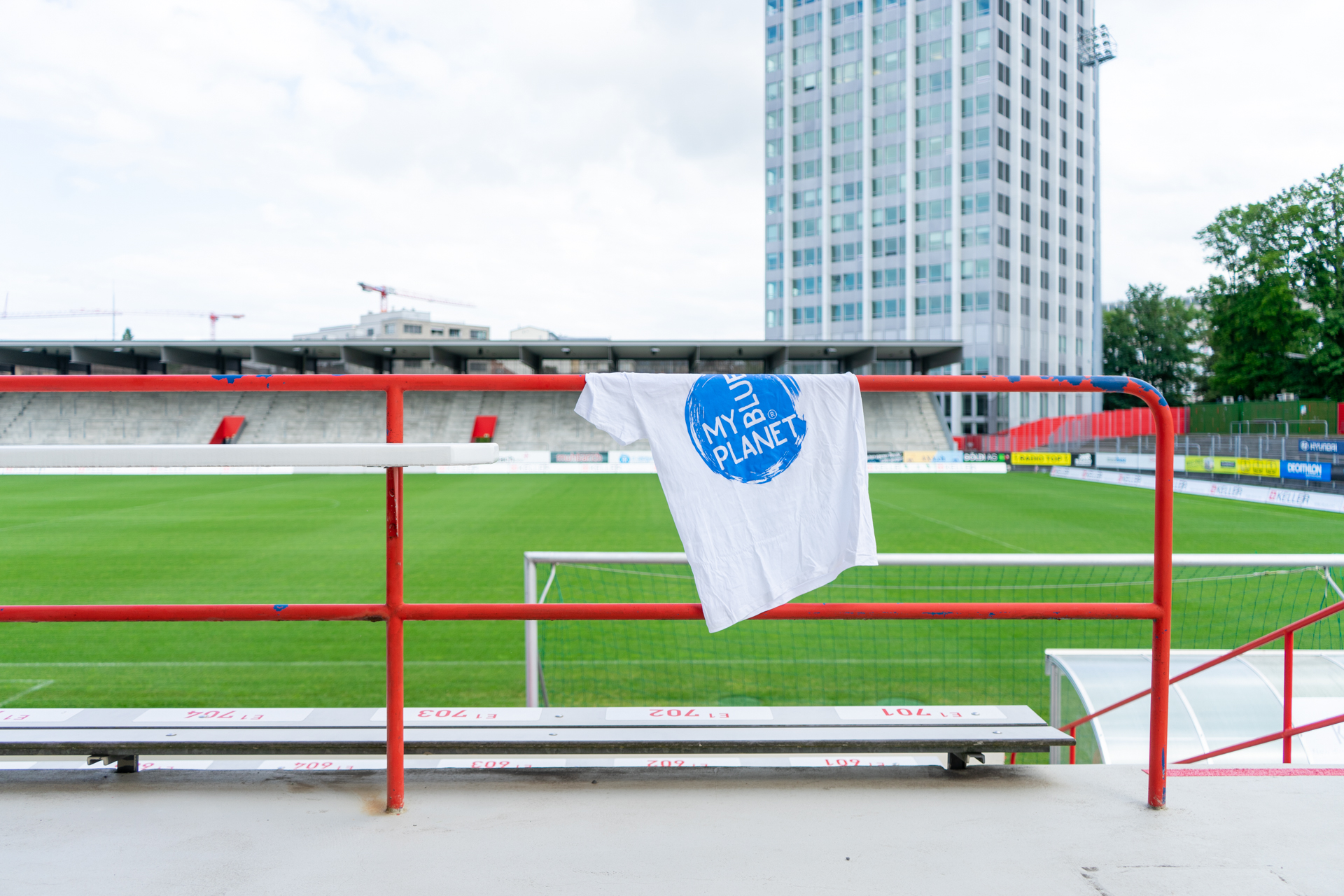 MYBLUEPLANET T-Shirt hängt an Stange beim Fussballfeld