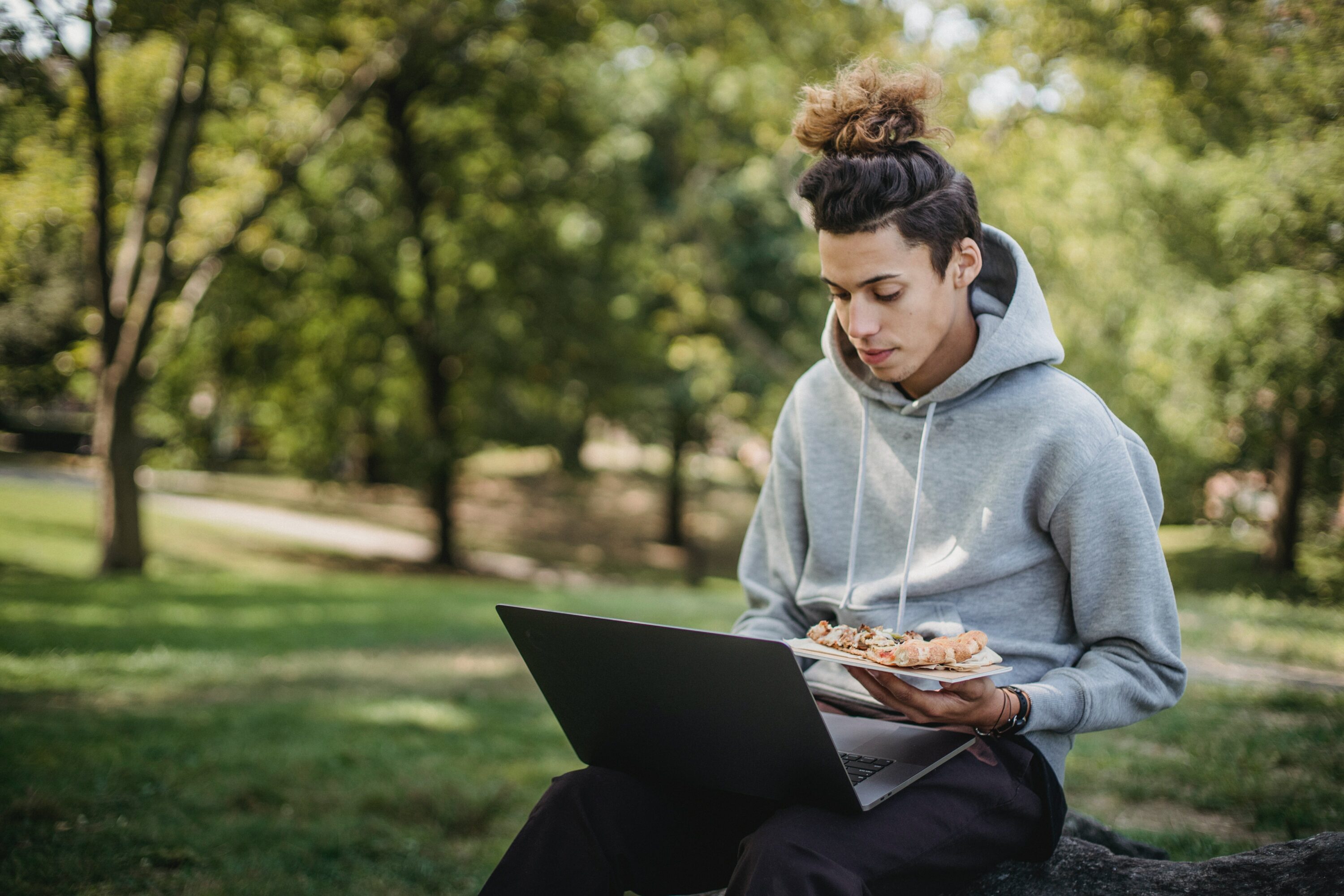 Mann beim Essen im Park und mit Laptop
